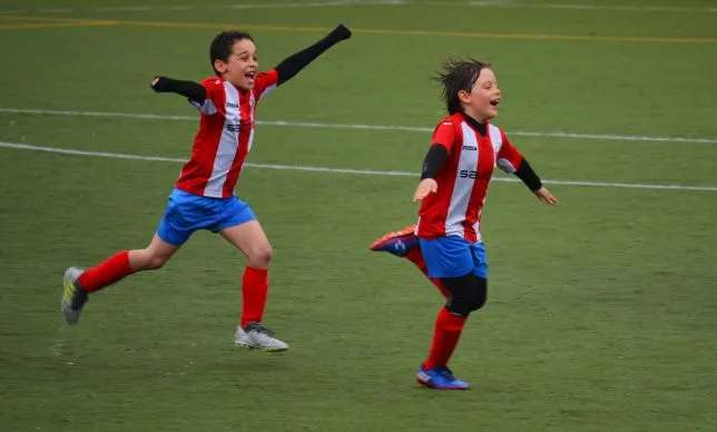 Młodzi piłkarze biegną na boisku, cieszą się ze strzelonej bramki